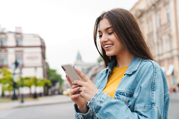 Image of woman smiling and using smartphone while walking on city street