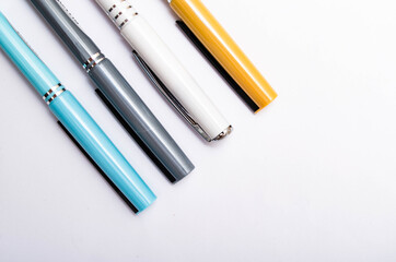 Four pens of blue, white, orange and gray are on a white background from above, from the side, at an angle. Four pens in close-up on a white background. Caps from pen