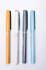 Four pens of blue, white, orange and gray are on a white background from above, from the side, at an angle. Four pens in close-up on a white background. Caps from pen