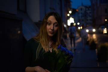 Fototapeta na wymiar Girl with a bouquet of blue flowers in the evening on the street.