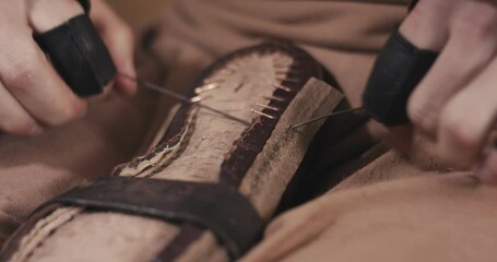 Traditional bespoke shoemaker tighten knot sewing stitching leather upper to insole on wooden shoe last with thread gloves on hands unrecognizable close up slow motion