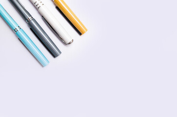 Four pens of blue, white, orange and gray are on a white background from above, from the side, at an angle. Four pens in close-up on a white background. Caps from pen