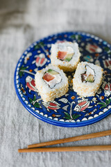 Sushi rolls on a blue plate with chopsticks on a gray background. Stylish composition with sushi.