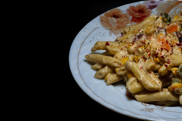 Pasta with white sauce and cheese placed in a plate in a dark background