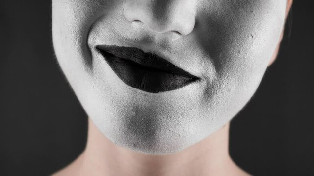 Portrait of a mime and bodypainting woman in white with black lips. Woman's lips on black background close-up