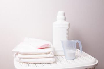 Obraz na płótnie Canvas the concept of washing white linen, bleach and detergent on a white laundry basket, a stack of white linen and baby socks, light background, copy space