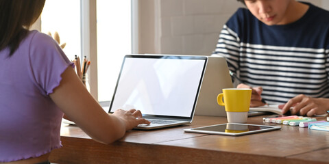 A young woman is typing on a computer laptop while sitting together with her colleague.