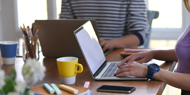A young woman is typing on a computer laptop while sitting together with her colleague.