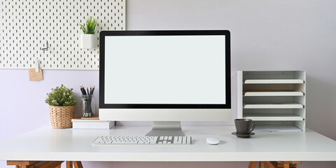 A white working desk is surrounding by a white blank screen computer monitor and office equipment.