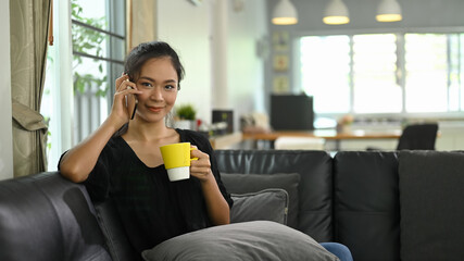 A young woman is talking on a telephone while sitting on a leather sofa.