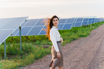 Girl walk between 2 Solar panels row on the ground at sunset. Woman investor wears formal white shirt. Free electricity for home. Sustainability of planet. Green energy.