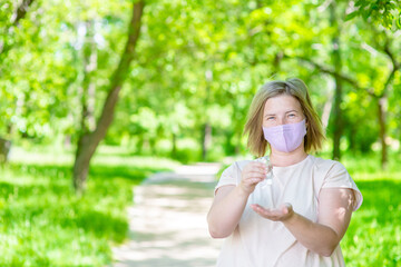 Woman wearing medical protective mask stands in public place and applies an antibacterial antiseptic gel for hands disinfection and cleaning during flu virus outbreak, coronavirus epidemic and infecti