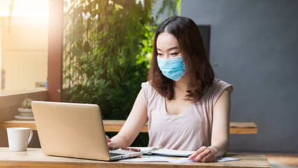 Asian woman wearing medical mask for healthcare and protection from virus, working from home, or in the coffee shop.  New Normal lifestyle to protect infection from Coronavirus, Covid-19.