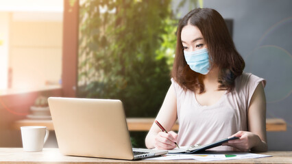 Asian woman wearing medical mask for healthcare and protection from virus, working from home, or in the coffee shop. New Normal lifestyle to protect infection from Coronavirus, Covid-19.