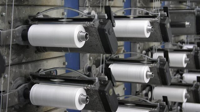 Rows of white reels with ropes making plastic sacks in a modern production plant