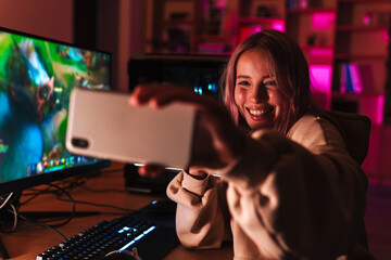 Image of girl taking selfie on cellphone while playing video game