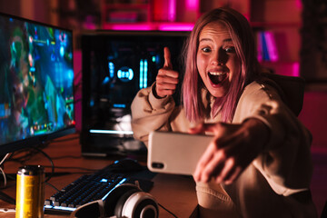 Image of girl taking selfie on cellphone while playing video game