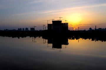 Beautiful urban construction site silhouettes at Dawn. Morning Cityscape with Reflection in lake water.