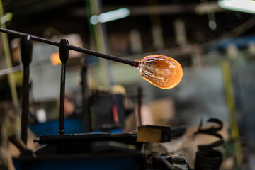 Fototapeta na wymiar Beautiful close-up of glassblower craftsman artist's shaping the piece of molten glass in his workshop. International workers day / Labour day.
