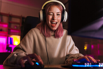 Image of excited girl in headphones winking and playing video game