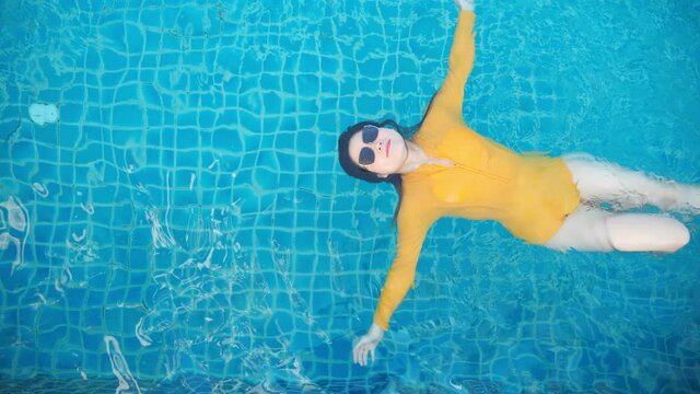 Summer Vacation, View from the top of asian woman in a yellow swimsuit swims backstroke in the pool. Asian woman relaxing sunbathing enjoying travel holidays at resort pool. Luxury lifestyle.
