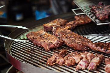 Fresh grilled meat. Street market. Chef preparing meat, close up. Chef with tongs holding hot pork ribs. Street food.