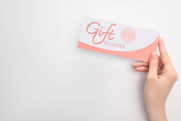 Top view of woman holding gift voucher with 10 dollars sign on white surface
