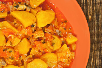 Potatoes in a green plate on a wooden table. Boiled potatoes with orange sauce on a brown board.