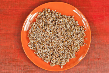 Buckwheat orange plate on a wooden table. Food in utensils on a background of old red plywood. Place for text near the plate. Copy space for design.