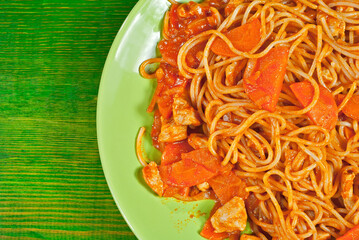 Pasta with carrots and meat in a green plate on a wooden table. Vermicelli with orange sauce on a shabby board. Place for text near the plate. Copy space for design.