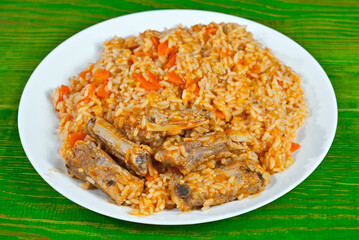 Pilaf with meat and carrots in a white plate. Rice on an old green board.