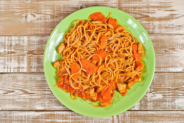 Pasta with carrots and meat in a green plate on a wooden table. Vermicelli with orange sauce on a pink shabby board. Place for text near the plate. Copy space for design.
