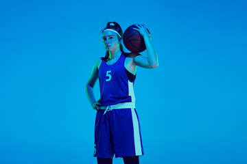 Young caucasian female basketball player of team posing confident with ball isolated on blue...