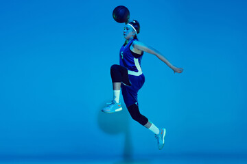 Fototapeta na wymiar Leader. Young caucasian female basketball player training, prcticing with ball isolated on blue background in neon light. Concept of sport, movement, energy and dynamic, healthy lifestyle.
