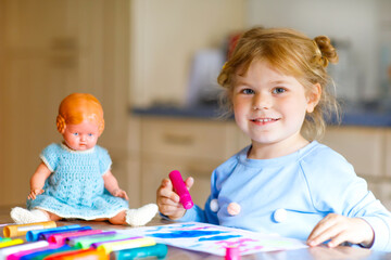 Fototapeta premium little alone toddler girl painting with felt pens during pandemic coronavirus quarantine disease. Happy creative child with old vintage doll, homeschooling and home daycare with parents
