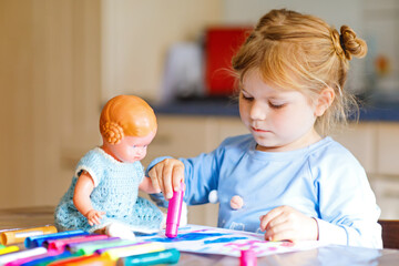 little alone toddler girl painting with felt pens during pandemic coronavirus quarantine disease. Happy creative child with old vintage doll, homeschooling and home daycare with parents