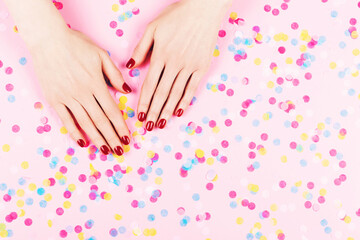 Plakat Manicure and nailcare concept. Two woman hands and falling confetti on pink background. Classic red polish. Flat-lay, top view. 