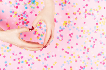 Manicure and nailcare concept. Two woman hands in heart shape and falling confetti on pink background. Classic red polish. Flat-lay, top view.  