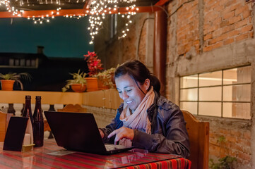 Woman is working smiling with a laptop on a hotel terrace at night lit by Christmas lights
