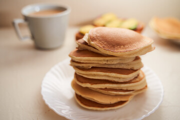Homemade pancakes are on the table. Nearby is a mug of coffee with milk. Light background