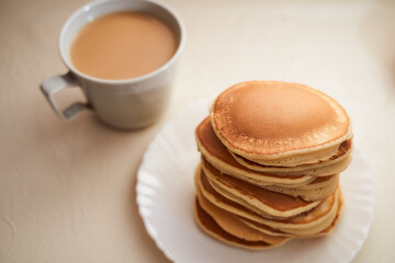 Homemade pancakes are on the table. Nearby is a mug of coffee with milk. Light background