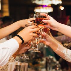 hands of a group of people clinking and toasting glasses of red wine at a festive party in a...