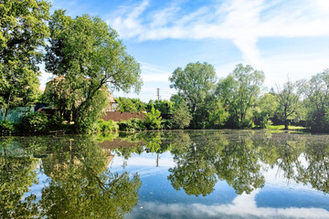 russian dacha house landscape with scenery reflection in pond water against blue sky background. Wide view of authentic countryside of russia. Summer in russian rural settlement