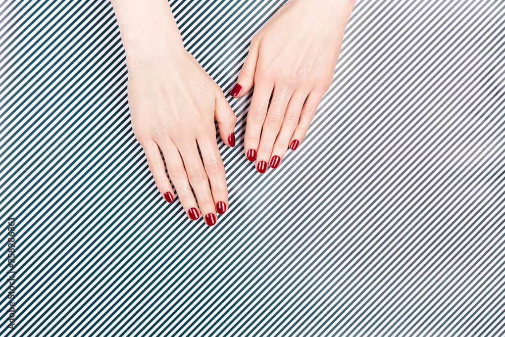 Wall mural Luxury manicure and nail care concept. Two woman hands with perfect red polish nails on black and white striped background. Classic and elegant design. Flat-lay, top view.