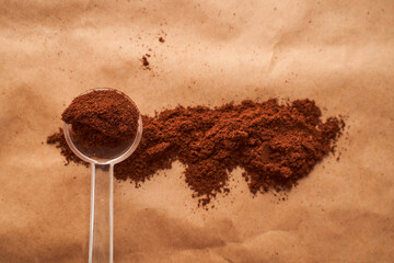plastic spoon with ground coffee in the shape of a rectangle on a brown background