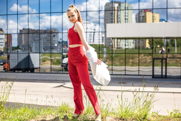 young blonde schoolgirl in a red suit and a white jacket posing in the parking lot