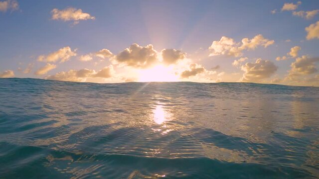 SLOW MOTION, LENS FLARE, CLOSE UP: Small ocean waves roll towards the camera on a sunny summer evening. Picturesque shot of a swell rolling towards the camera at beautiful summer sunset in Caribbean