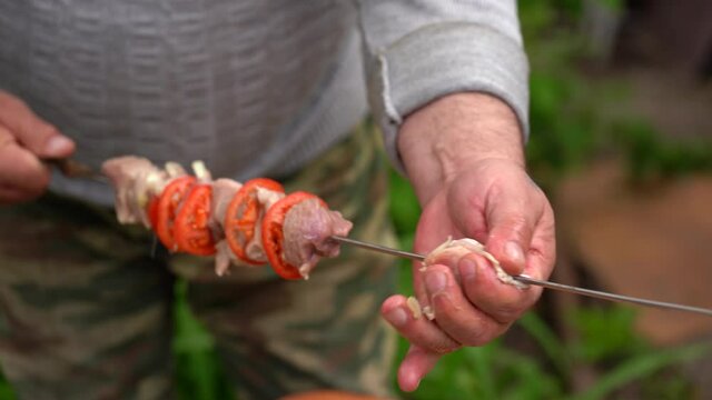 Mature man impales raw shashlik on skewer. Close up of men's hands hold skewer with barbecue. Concept of picnic outdoor.