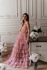 photo in the style of advertising expensive perfumes. a girl in a vintage studio dressed in a beautiful pink dress and surrounded by bouquets of fresh peonies