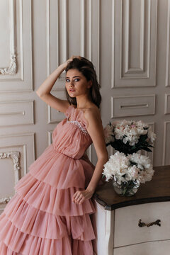 photo in the style of advertising expensive perfumes. a girl in a vintage studio dressed in a beautiful pink dress and surrounded by bouquets of fresh peonies